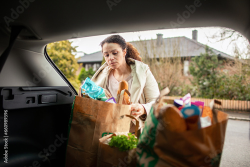 Young woman taking groceries out of the trunk in the driveway of her home photo