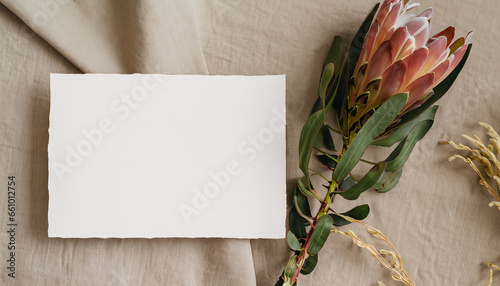 Luxurious boho-style invitation card template featuring a blank paper and a protea flower on a beige linen cloth, allowing space for custom text photo