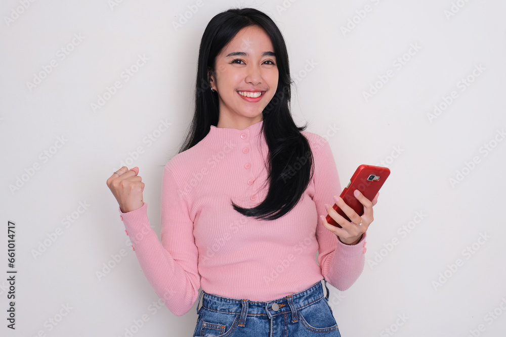 Young Asian woman smiling and clenched fist while holding mobile phone Young Asian woman smiling and clenched fist while holding mobile phone