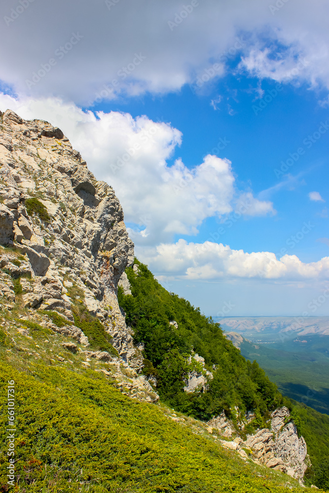 steep rocky cliff in the Crimean mountains in Europe against the backdrop of distant hills and a blue sky with clouds
