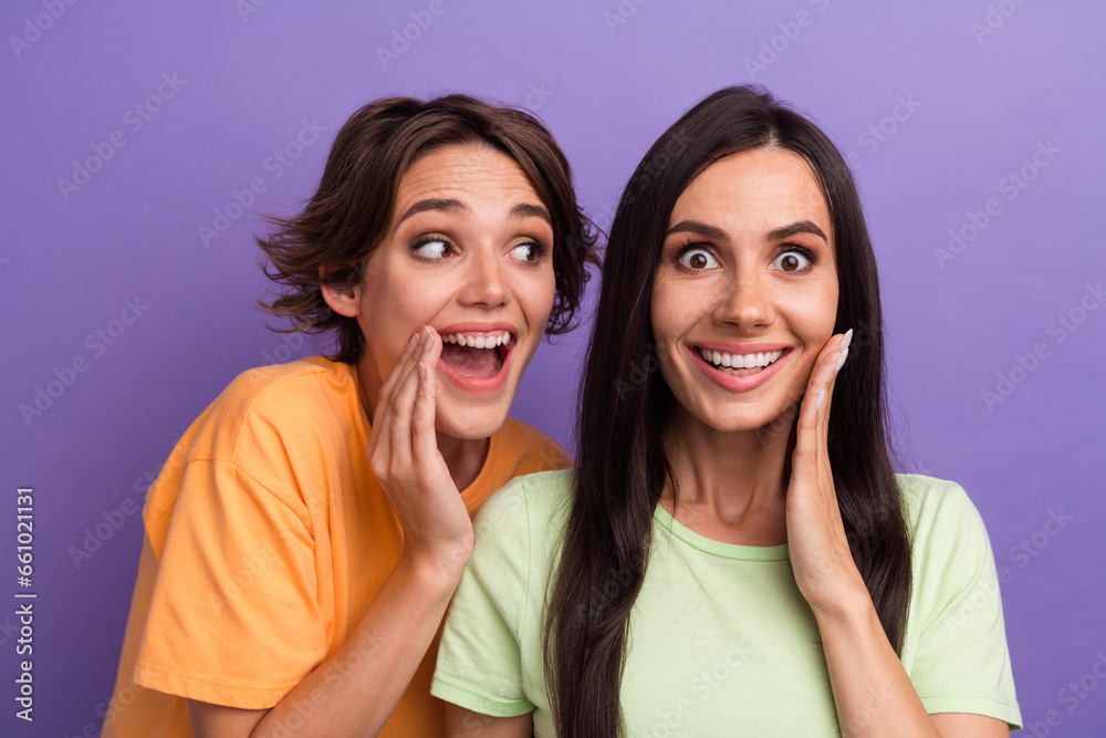 Photo of excited impressed ladies wear t-shirts smiling arm cheek listening secrets isolated violet color background Photo of excited impressed ladies wear t-shirts smiling arm cheek listening secrets isolated violet color background