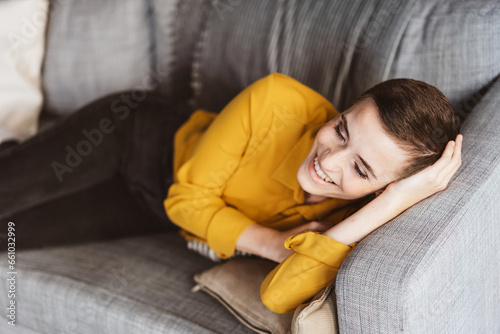 фотографія Young Woman with Short Hair Laughing on Sofa in Modern Apartment