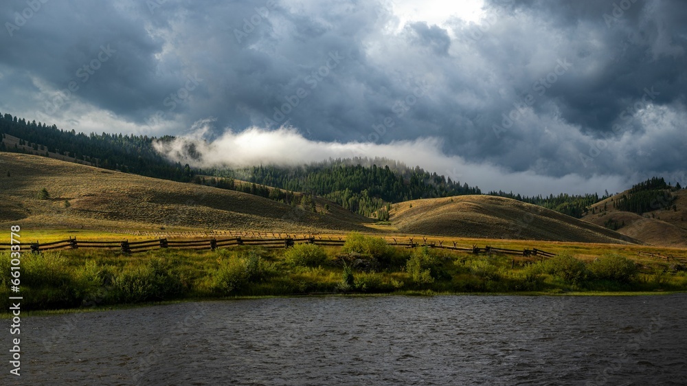 clouds hover over a pasture with a lake on the bank