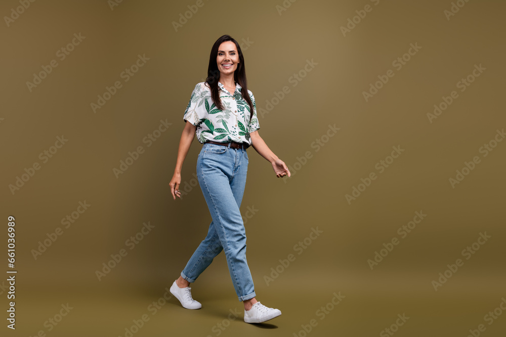 Full size profile portrait of satisfied glad young girl walking empty space ad isolated on brown color background Full size profile portrait of satisfied glad young girl walking empty space ad isolated on brown color background