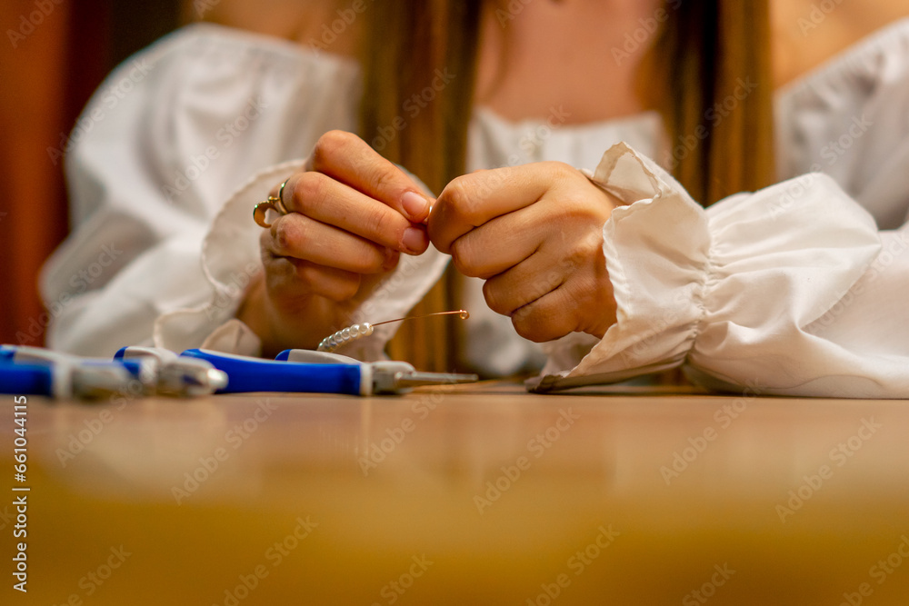 Obraz premium close-up hands of a young girl makes jewelry with her own hands strings beads on a wire for a necklace hobby