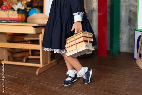 School Girl in dress holds a stack of books. Back to school. Little girl with books stand near of chalkboard. Kid is studying in the classroom on the background of school board. 