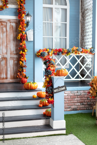 Residential house decorated for Halloween holiday. Different colored pumpkins in front door On Wooden Steps. Porch of yard decorated with orange pumpkins in autumn. Thanksgiving. Halloween outside. 