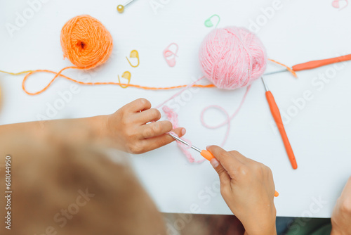 Mom teaches her daughter to knit. Mom and a little blonde girl are sitting at the table and crocheting.