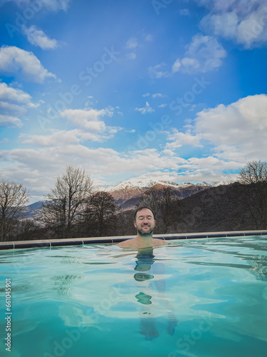 happy man in an infinity pool with warm water against the backdrop of snow-capped mountain peaks
