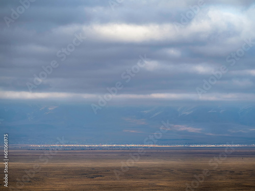 Thin line of a distant city in the steppe under a blue cloudy sky. Altai steppe.