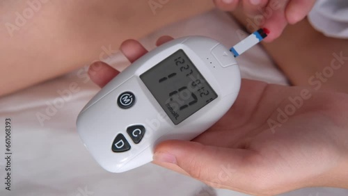 Teenage girl measures blood glucose level on bed at home.