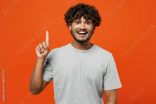 Young insighted smart proactive happy Indian man he wears t-shirt casual clothes holding index finger up with great new idea isolated on orange red color background studio portrait. Lifestyle concept.