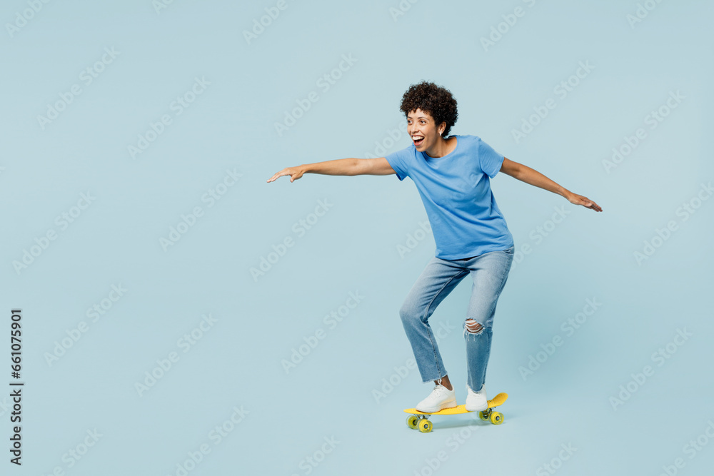 Full body side profile view young woman of African American ethnicity wear t-shirt casual clothes riding skateboard pennyboard isolated on plain pastel light blue cyan background. Lifestyle concept.