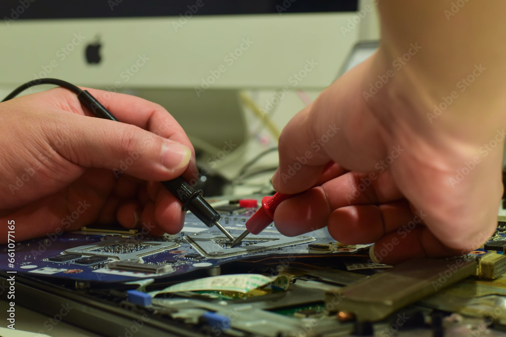 computer technician A laptop motherboard repairman is using an IC meter to find defects on the motherboard to repair on his table. Board repair using modern technology computer technician A laptop motherboard repairman is using an IC meter to find defects on the motherboard to repair on his table. Board repair using modern technology