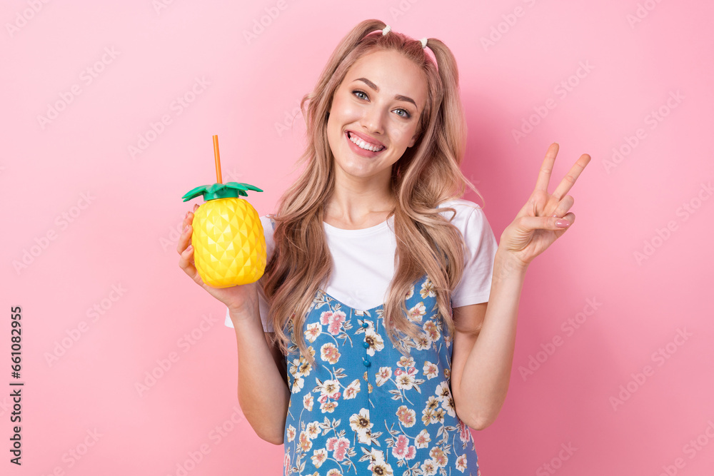 Portrait of pretty positive girl hold pineapple juice cup demonstrate v-sign isolated on pink color background Portrait of pretty positive girl hold pineapple juice cup demonstrate v-sign isolated on pink color background