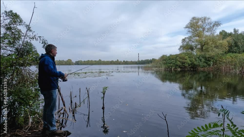 A professional fisherman, a young man, uses a spinning rod to catch fish on the seashore in the mountains, throwing gear far into the water and winding up the fishing line and rotating the reel. A professional fisherman, a young man, uses a spinning rod to catch fish on the seashore in the mountains, throwing gear far into the water and winding up the fishing line and rotating the reel.