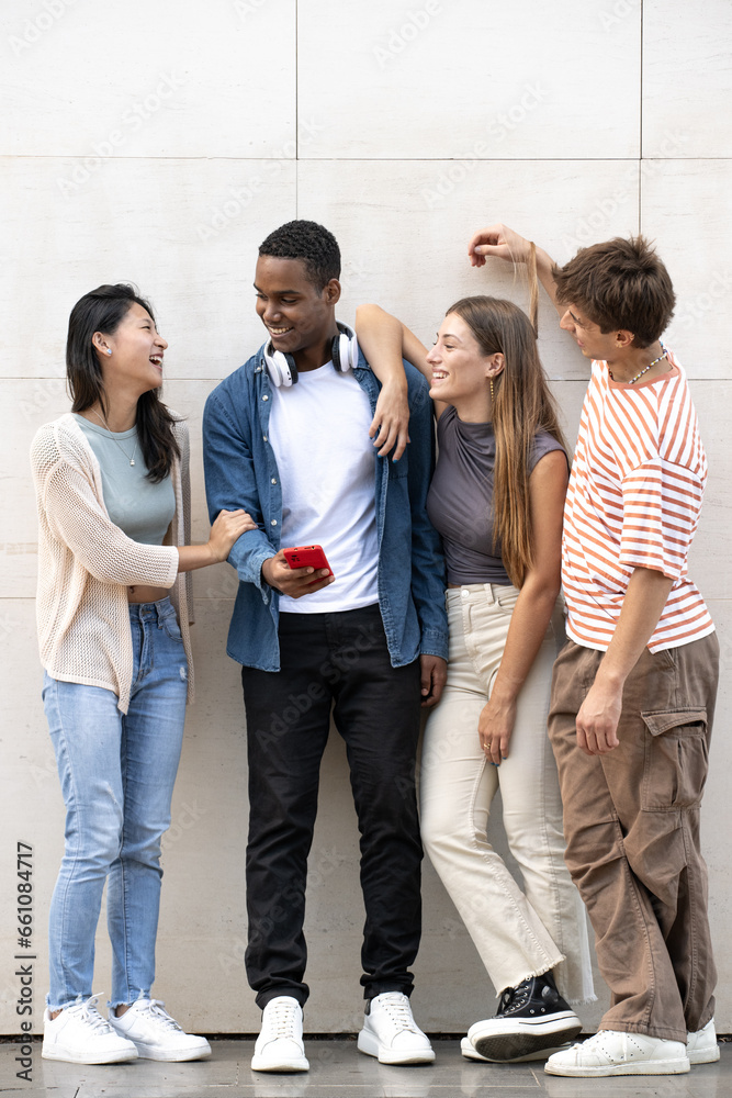 Young diverse group laughing together leaning against a grey wall.Cheerful men and women talking and having fun outside.