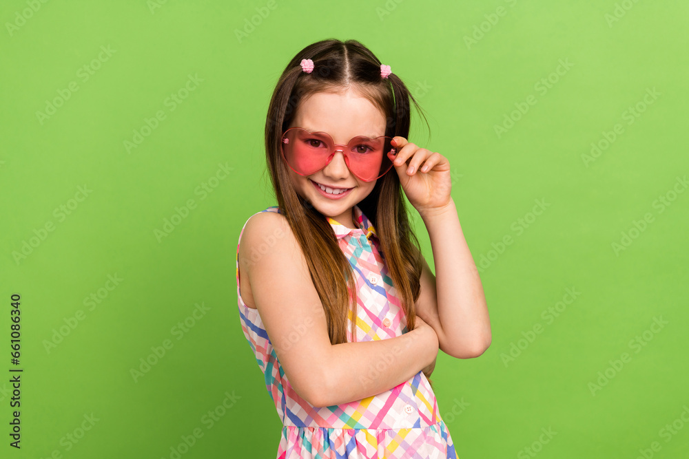 Portrait of adorable satisfied schoolkid toothy smile hand touch heart shape sunglass isolated on green color background