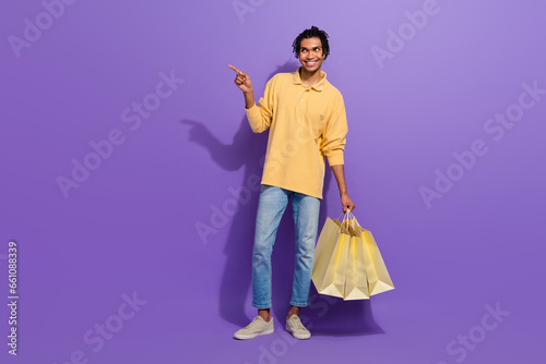 Full body photo of shopaholic guy wear shirt denim jeans indicate finger mockup store bags gucci isolated on purple color background