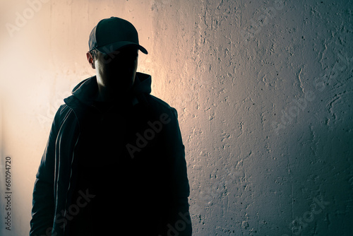 Criminal, suspicious stranger or stalker. Person with face in dark shadow. Anonymous man, terrorist suspect or gangster silhouette figure. Urban grunge background. Young thief hiding incognito. photo