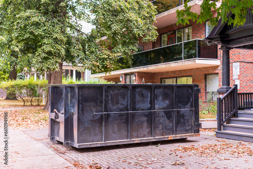 Canvas Print A roll-off construction dumpster, black side view,outside a residential renovation project in an older neighourhood