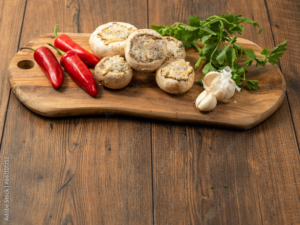 Stuffed mushrooms cups and chilly peppers and garlic cloves on a wooden board and table. High quality product with breadcrumbs, cheese and herbs ready for oven cooking. Stuffed mushrooms cups and chilly peppers and garlic cloves on a wooden board and table. High quality product with breadcrumbs, cheese and herbs ready for oven cooking.
