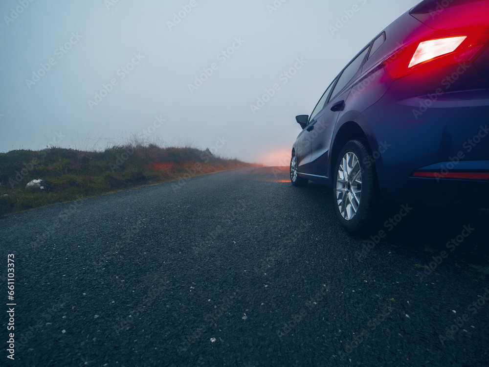 Car on a small narrow country road with high quality asphalt surface without marking at fog. Driving in dangerous conditions due to poor weather and low visibility in rural area. Selective focus.