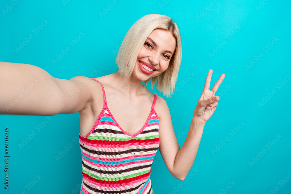 Selfie of smiling blogger youngster woman blonde hair show v sign greetings wear glamour singlet isolated on aquamarine color background Selfie of smiling blogger youngster woman blonde hair show v sign greetings wear glamour singlet isolated on aquamarine color background