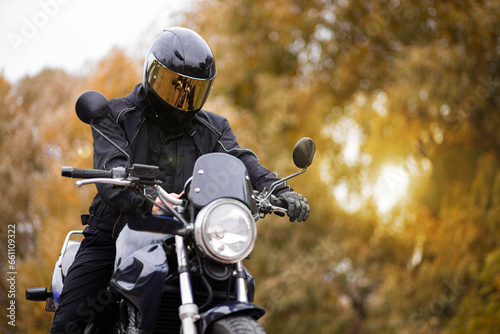 motorcyclist in motorcycle gear and helmet near a classic motorcycle in autumn