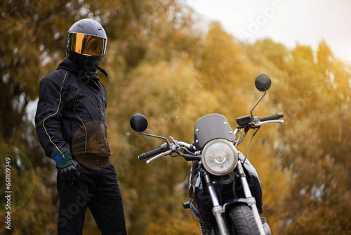 motorcyclist in motorcycle gear and helmet near a classic motorcycle in autumn © velimir