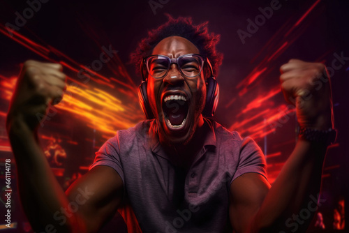 Excited african american gamer shouting yes with raising hands and clenched fists after winning Esports competition isolated on dark background with colorful yellow and red lights.