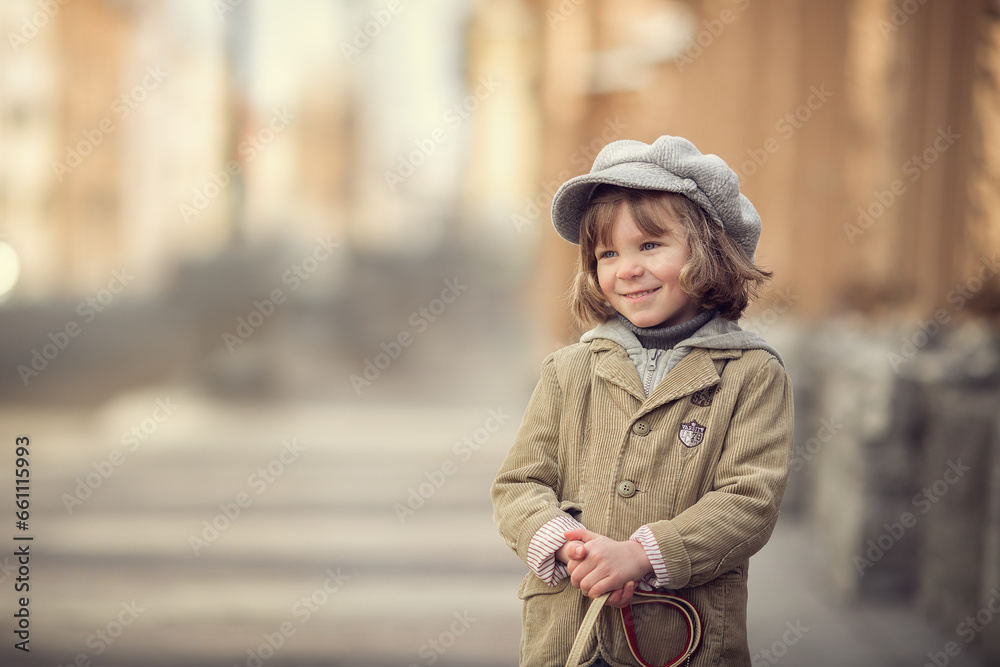Fototapeta premium Little boy with long hair in grey hat on city street in spring smiling