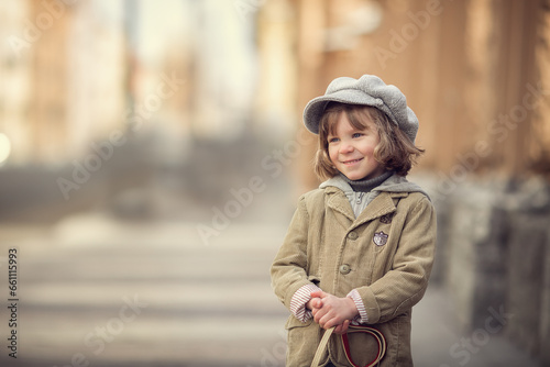 Little boy with long hair in grey hat on city street in spring smiling