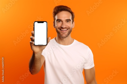 Portrait of young man advertising new smartphone showing it to camera against orange background