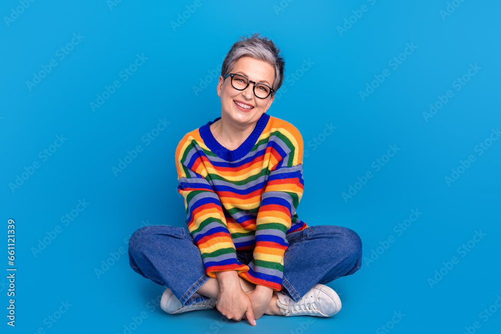 Full size portrait of satisfied glad aged person sit floor crossed legs have good mood isolated on blue color background Full size portrait of satisfied glad aged person sit floor crossed legs have good mood isolated on blue color background