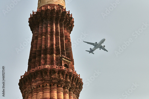 Qutb Minar minaret with airplane in sky background, tower part Qutb complex in South Delhi, India, big red sandstone minaret tower landmark popular touristic spot in New Delhi, tallest brick minaret photo
