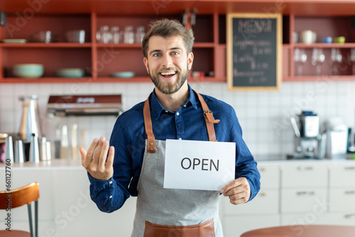 Successful small business owner man standing in coffee shop, keep the sign open and inviting to his cafeteria. SME entrepreneur seller business concept