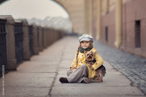 Girl in yellow coat and grey hat with a dog on city street 