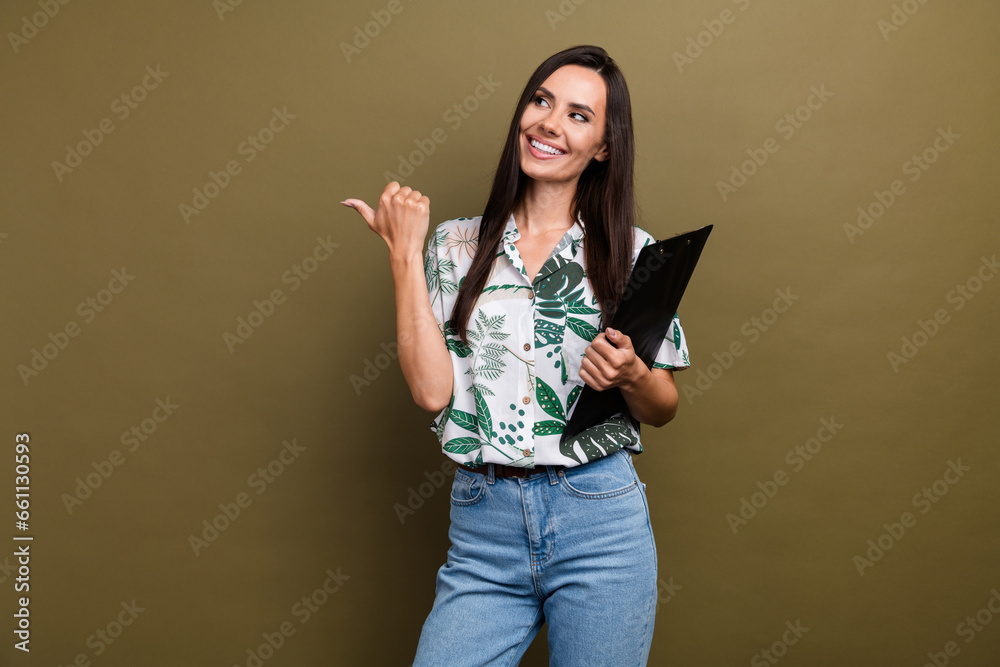Portrait of nice positive girl hold clipboard look direct finger empty space ad isolated on brown color background Portrait of nice positive girl hold clipboard look direct finger empty space ad isolated on brown color background