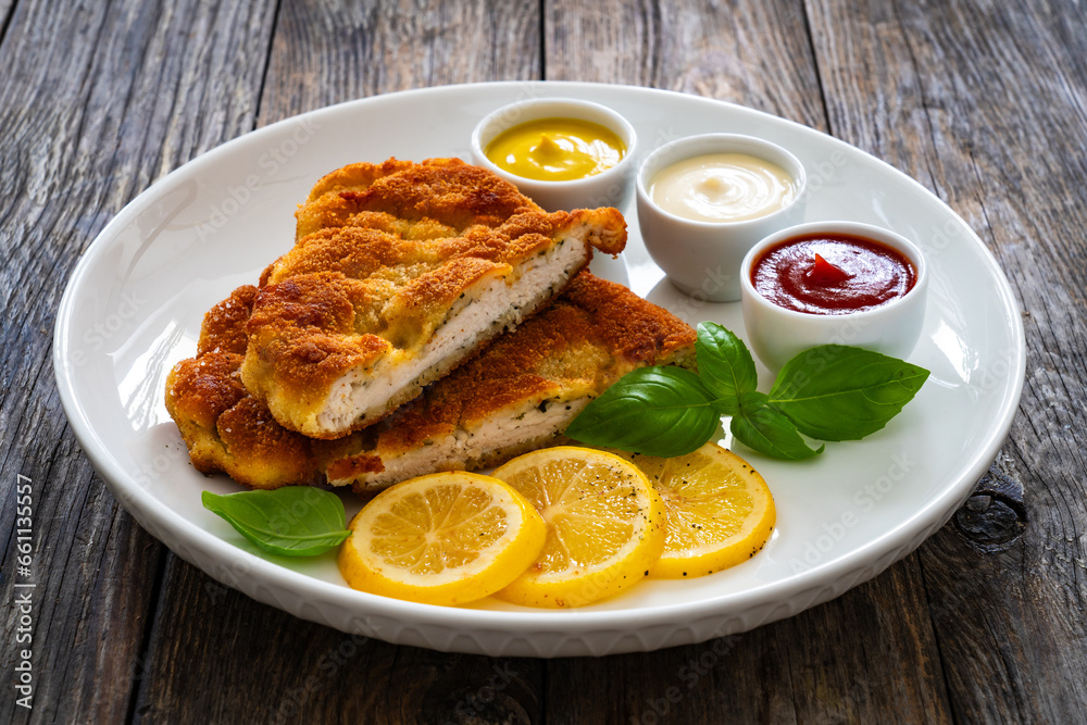 Crispy breaded seared chicken cutlet with lemon slices and fresh vegetables on wooden table
Crispy breaded seared chicken cutlet with lemon slices and fresh vegetables on wooden table