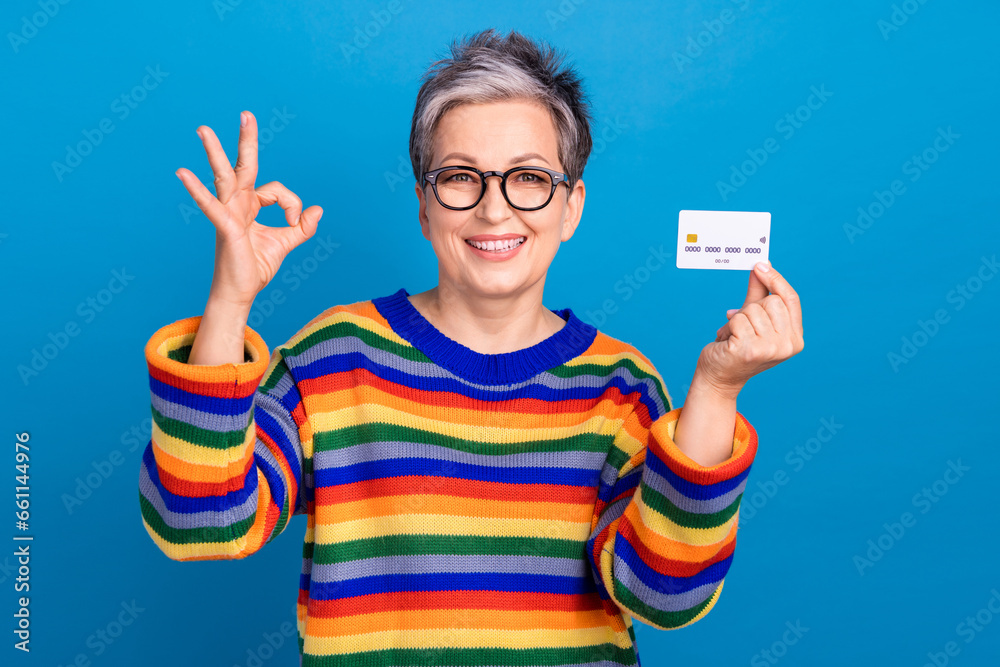 Photo of charming cheerful lady hold showing debit card demonstrate okey symbol isolated on blue color background Photo of charming cheerful lady hold showing debit card demonstrate okey symbol isolated on blue color background