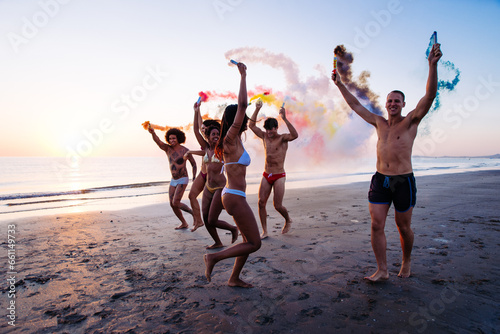 Group of friends having fun running on the beach with smoke bombs