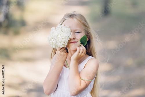 Portrait of a young beautiful girl who hides part of her face behind a hydrangea and smiles.