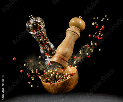 Fototapeta Naklejka Na Ścianę i Meble -  Mixed peppercorns in wooden bowl and spice mills flying over black background.