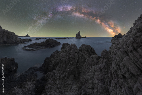 Picturesque landscape of rocks and mountains near calm sea under starry sky at night photo