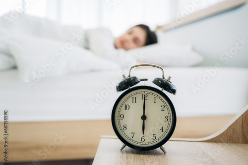 Close up of alarm clock on bedside table. Young Woman Waking Up with Happiness in Cozy Bedroom at Home. Beautiful Girl Smiling and Relaxing in Bed after Waking Up.