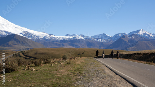 Winding highway among snow-covered mountains with a group of riders on horseback. Copy space.