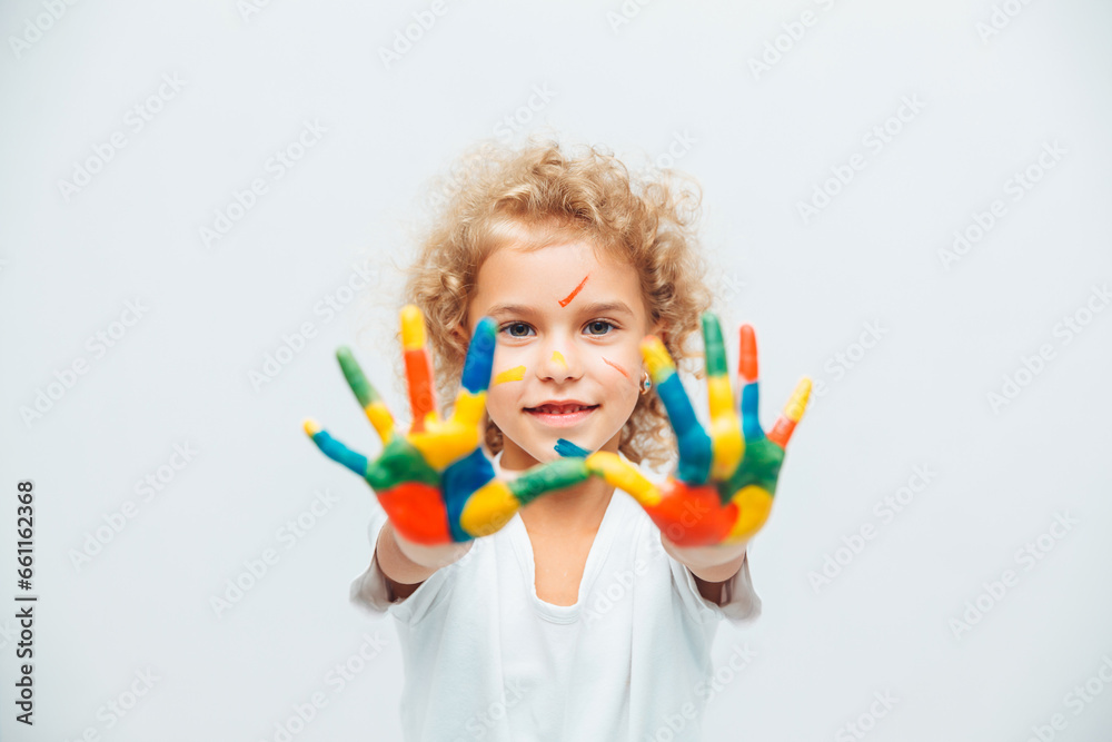 little blonde girl shows her hands painted with multi-colored paint on a white background. little blonde girl shows her hands painted with multi-colored paint on a white background.