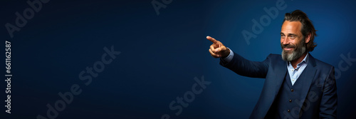 middle age man wearing formal clothes pointing to the side with finger and hand looking at the side in front a blue background. Banner design with space for text