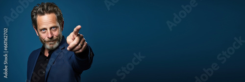 middle age man wearing casual clothes pointing with finger and hand to the side, looking at the camera against a blue background. Banner design with space for text